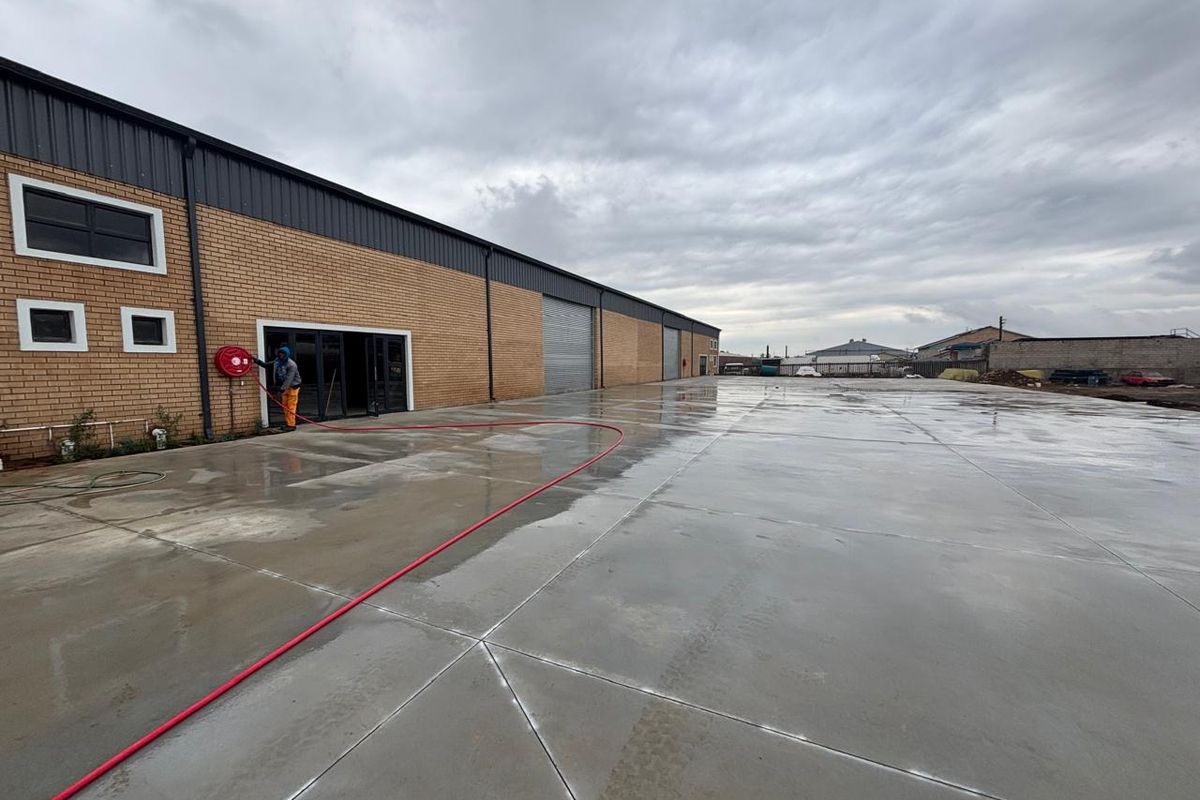 Spacious industrial rear yard featuring a large concrete surface, brick facade, and roller shutter access, suitable for logistics or storage operations.