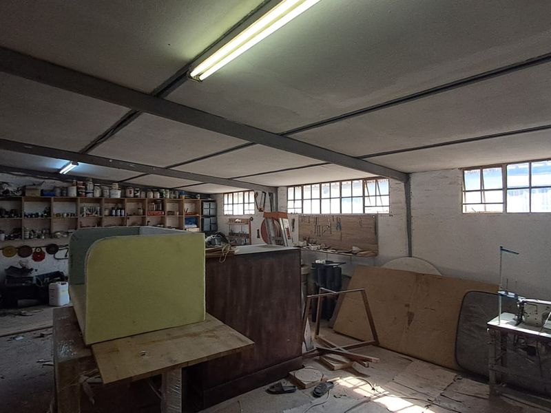 Spacious industrial utility area featuring exposed steel ceiling beams, built-in timber shelving, and multiple windows providing natural light.