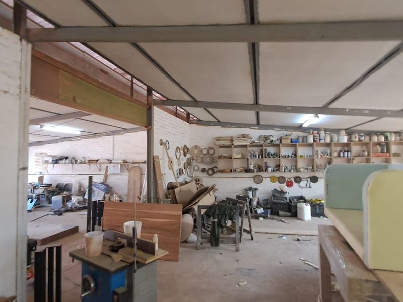 Industrial workshop space featuring exposed steel roof trusses, brick walls, and extensive built-in timber shelving for storage.