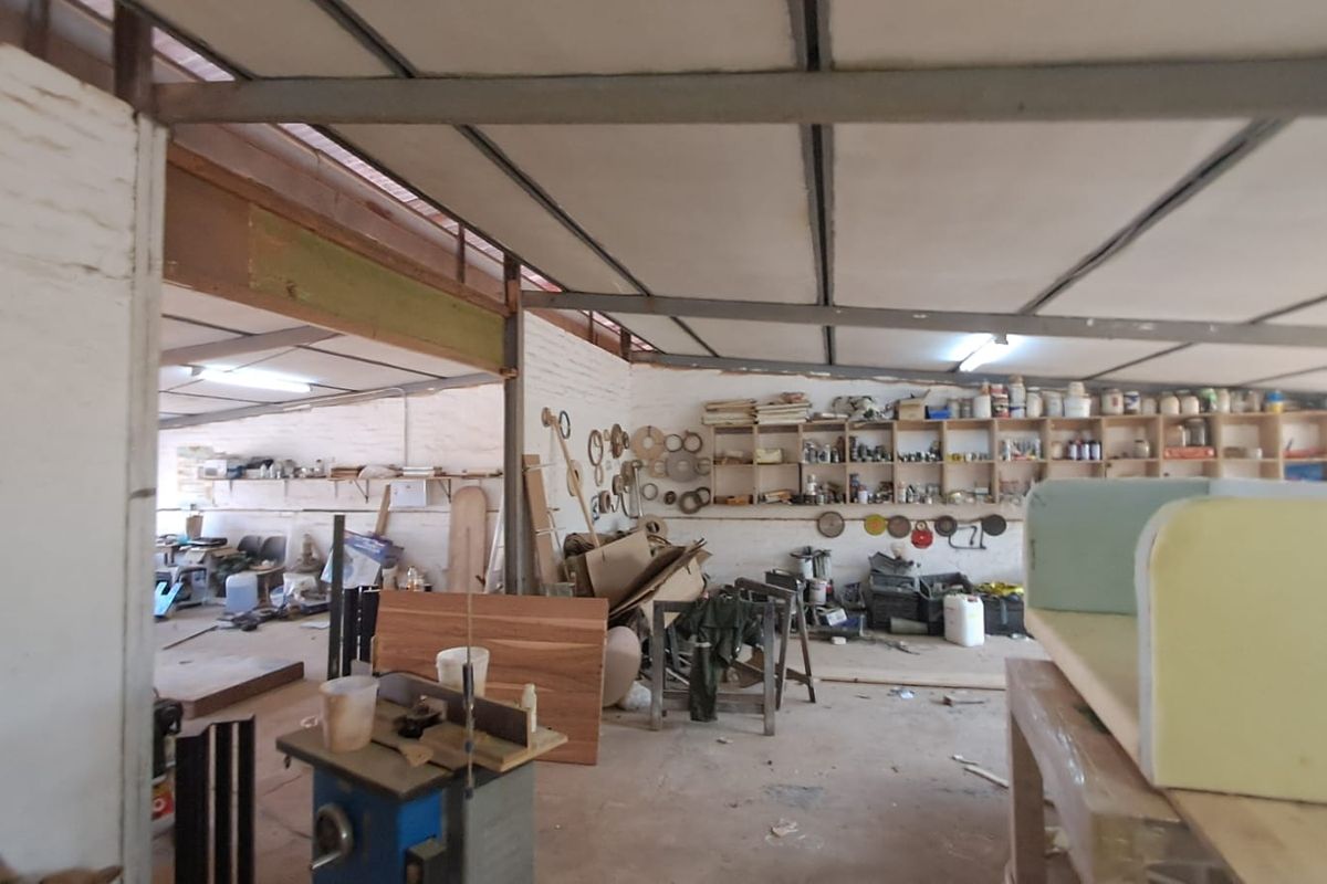Industrial workshop space featuring exposed steel roof trusses, brick walls, and extensive built-in timber shelving for storage.