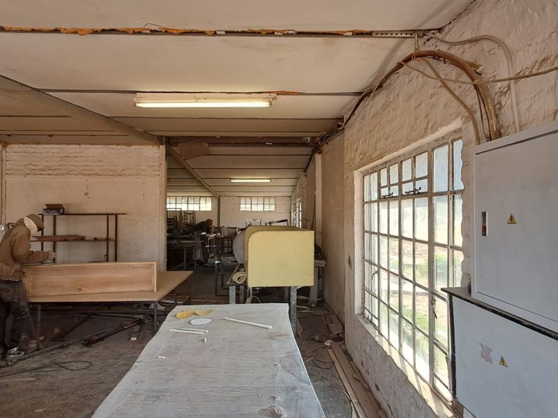 Industrial workshop space featuring exposed brick walls, steel-framed windows, and functional electrical infrastructure, suitable for manufacturing or storage use.