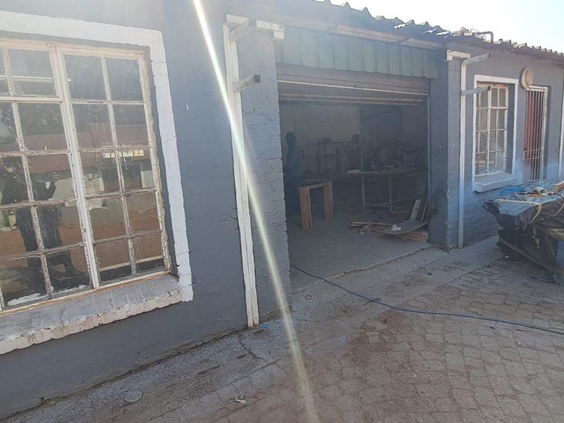 Industrial property exterior featuring a paved driveway, steel-framed windows, and a large roller shutter door access point.