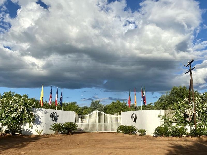 A gated entrance to the farm property featuring a white perimeter wall, metal security gate, and landscaped garden beds.