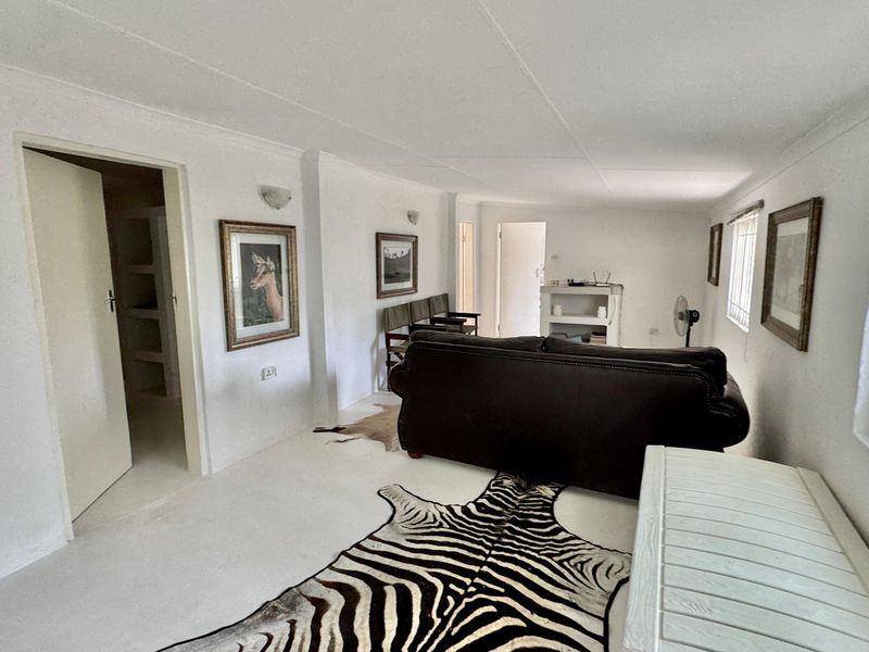 A simple living room area featuring white walls, tiled flooring, and security bars on the windows.