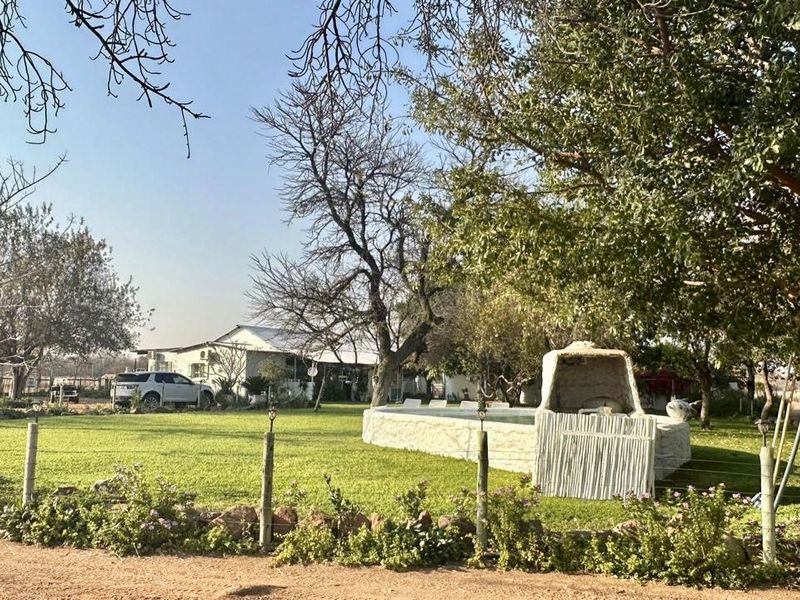 Outdoor pool area featuring a swimming pool, built-in braai, and expansive lawn set within a mature garden on the farm property.