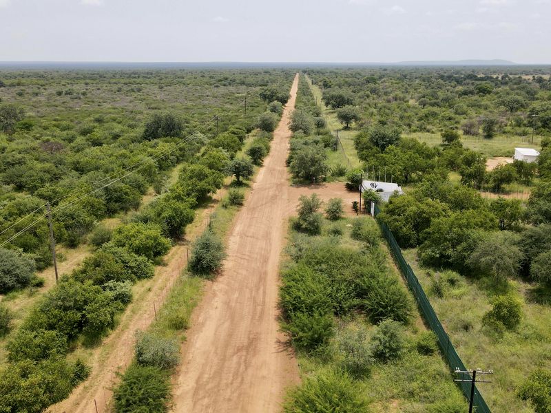 Aerial view of a rural farm property featuring a long dirt access road, surrounding bushveld vegetation, and existing perimeter fencing.