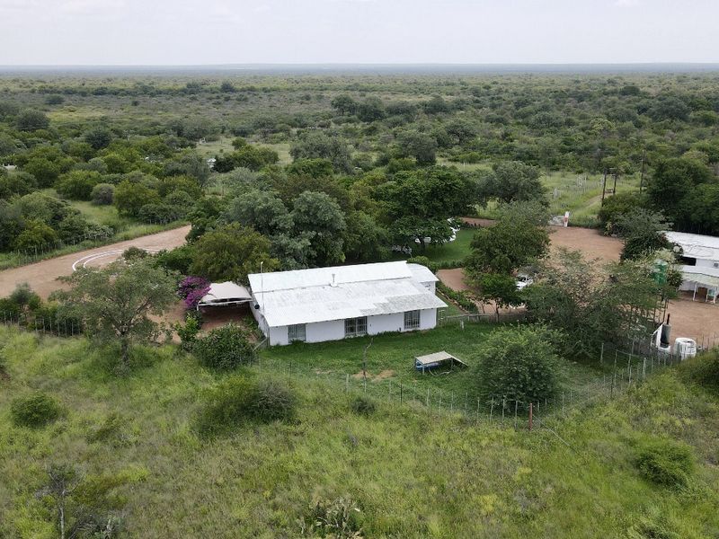 Aerial view of a rural farm property featuring a main dwelling with a metal roof, surrounding outbuildings, and extensive natural landscape.