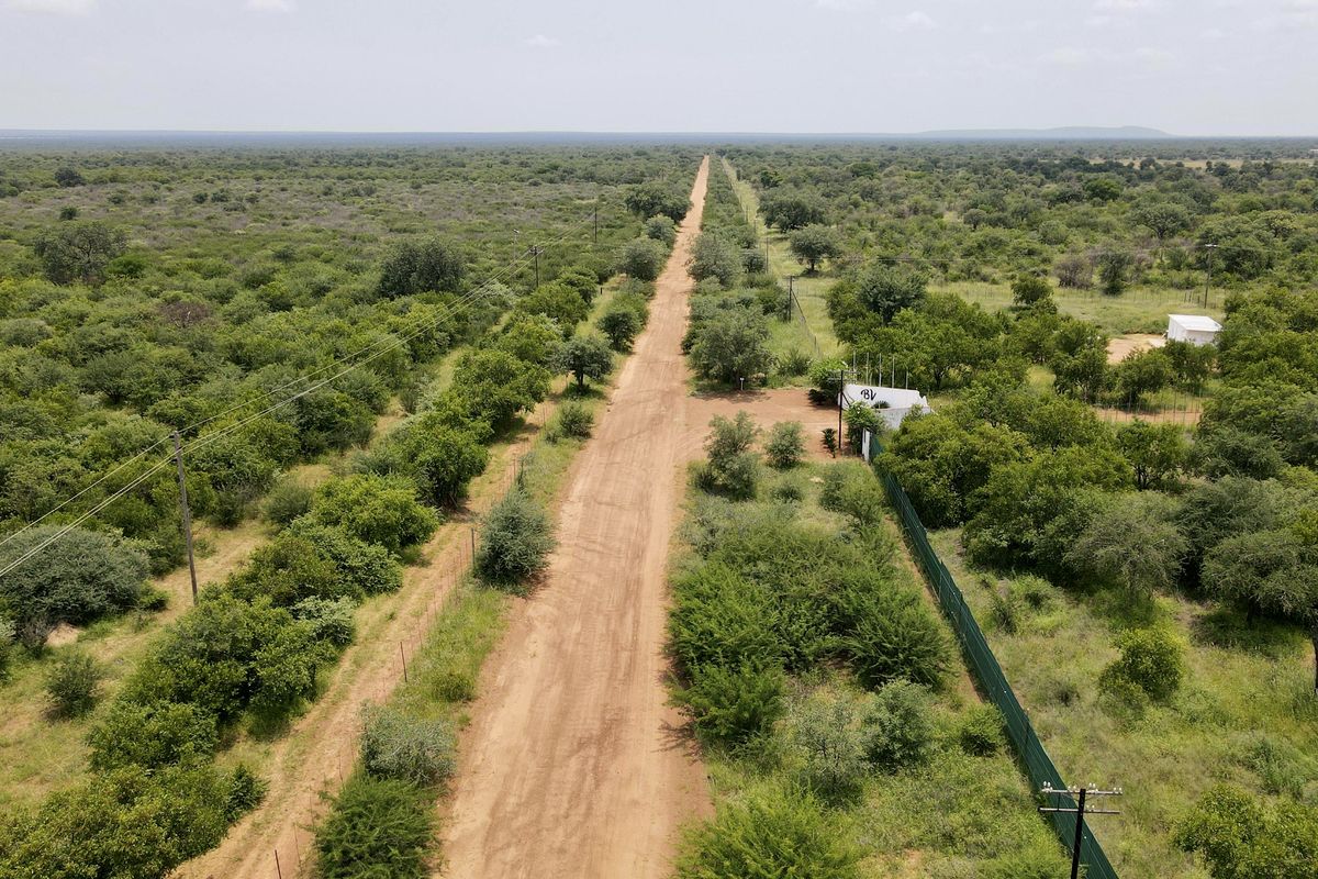 Aerial view of a rural farm property featuring a long dirt access road, surrounding bushveld vegetation, and existing perimeter fencing.