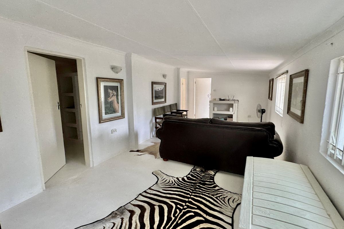 A simple living room area featuring white walls, tiled flooring, and security bars on the windows.