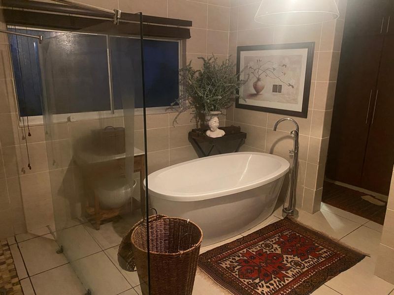A well-appointed bathroom featuring a modern freestanding bathtub with a floor-mounted filler, glass shower screen, and neutral wall tiling.