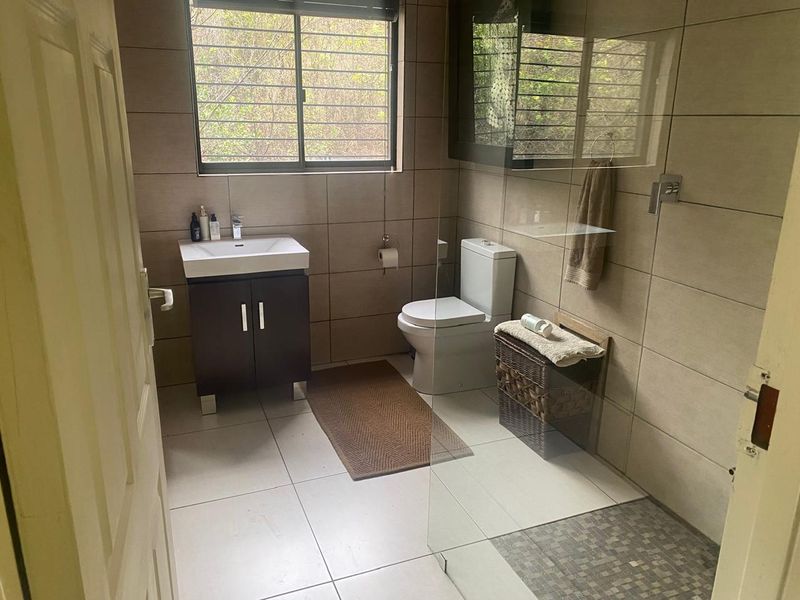 A modern bathroom featuring a vanity cabinet, toilet, and a walk-in shower with a glass screen and tiled flooring.