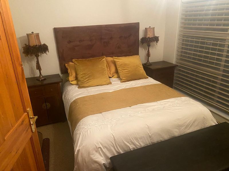A cozy bedroom featuring neutral walls, timber door, and venetian blinds, providing a functional and comfortable sleeping space.