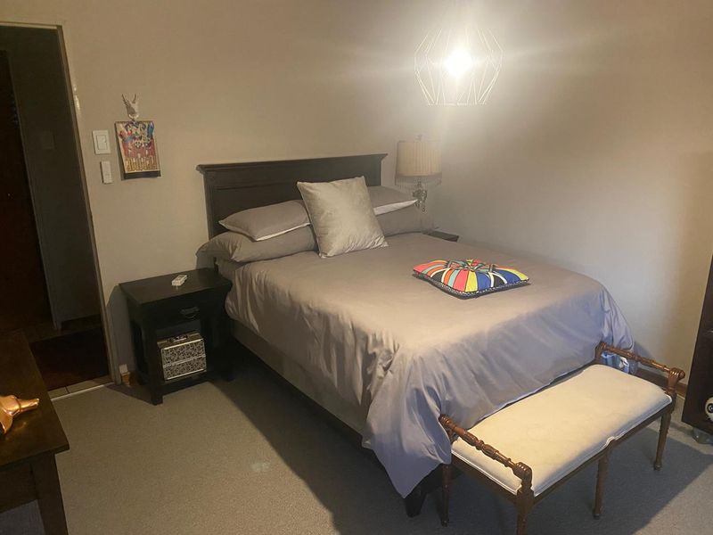 A standard bedroom featuring neutral wall tones, carpeted flooring, and a central pendant light fixture.