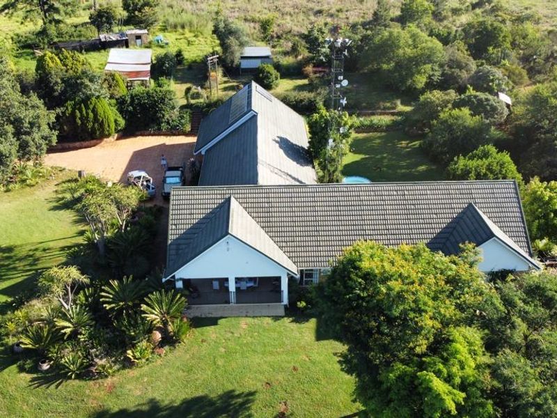 Aerial view of a farm property featuring a main residence with a tiled roof, covered patio, paved driveway, and surrounding landscaped grounds.
