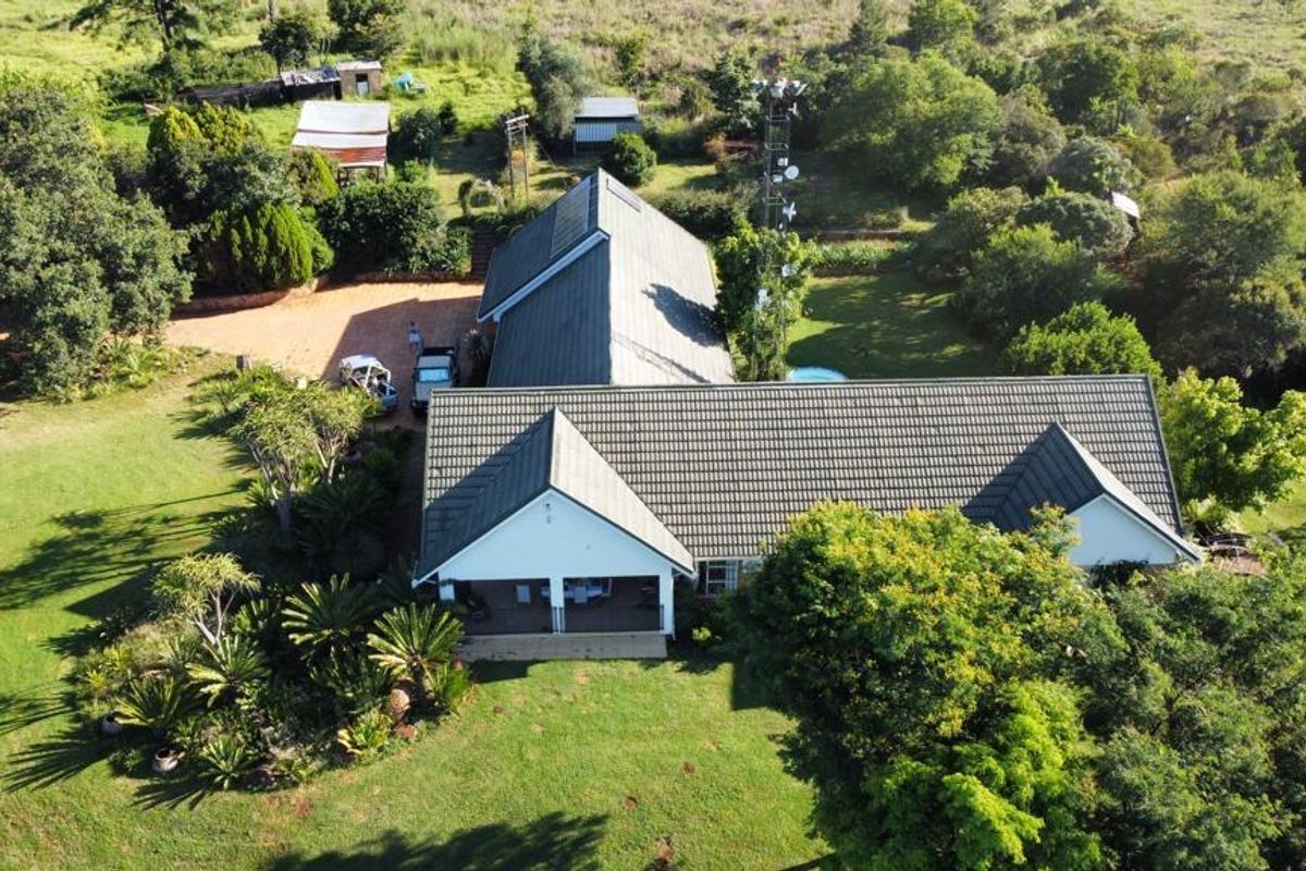 Aerial view of a farm property featuring a main residence with a tiled roof, covered patio, paved driveway, and surrounding landscaped grounds.