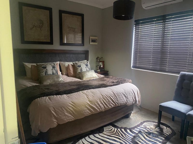 A well-maintained bedroom featuring a wall-mounted air conditioning unit and venetian blinds, providing a comfortable and functional living space.