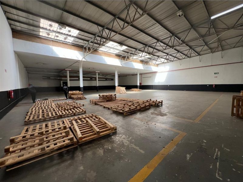 Spacious industrial warehouse area featuring high ceilings with exposed steel trusses, natural light from skylights, and durable concrete flooring.