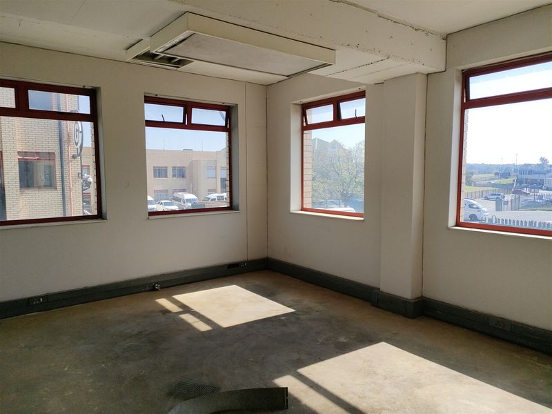 An empty industrial office space featuring exposed concrete floors, large windows with aluminium frames, and recessed ceiling lighting, offering a blank canvas for customization.