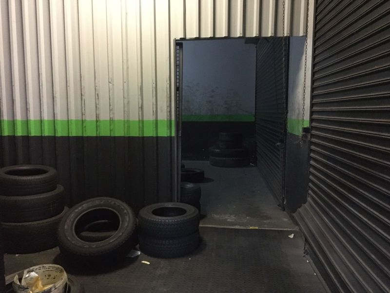 Commercial garage space featuring corrugated metal wall cladding, concrete flooring, and a secure roller shutter door entrance.