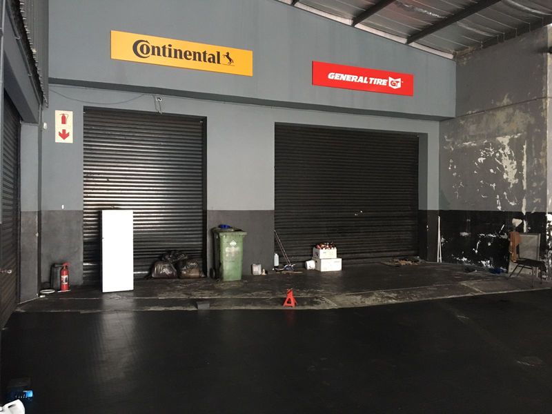 Commercial garage space featuring dual roller shutter doors, exposed metal roofing, and fire safety equipment, suitable for workshop or storage use.