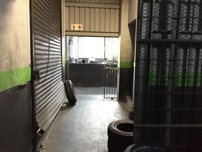 A functional utility or storage corridor featuring a metal roller shutter door, security gate, and durable rubberized flooring in a commercial setting.