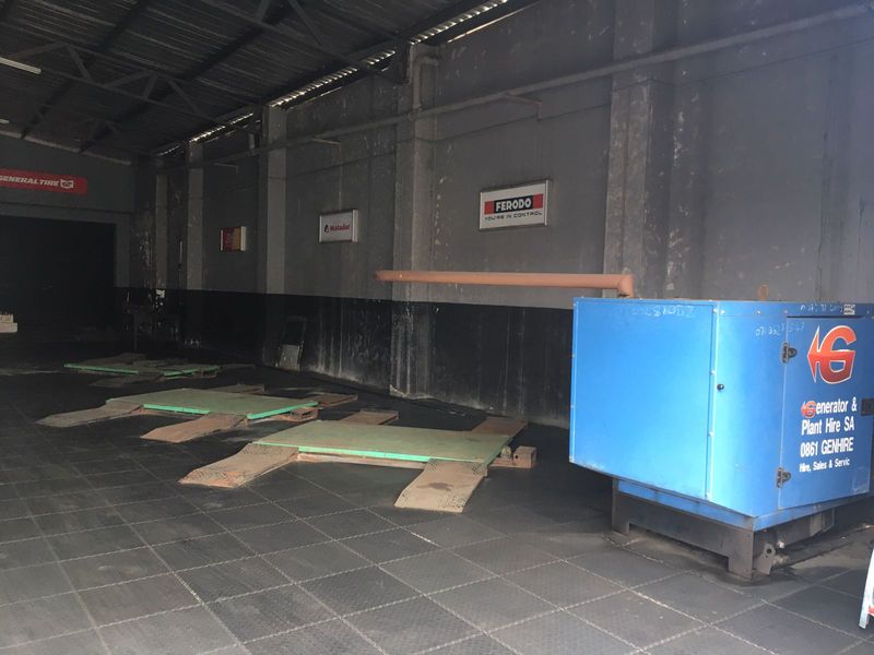Commercial garage space featuring industrial flooring, exposed steel roof structure, and multiple vehicle service bays for automotive maintenance operations.