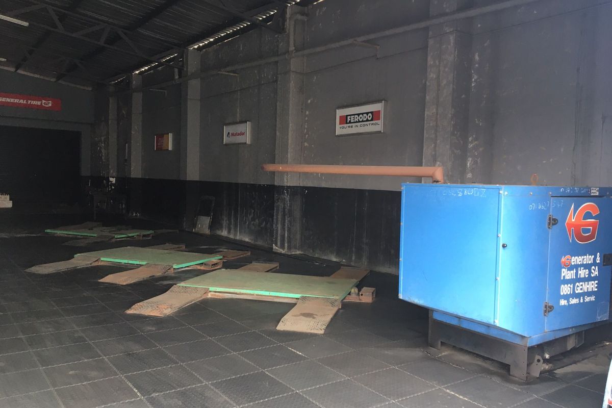 Commercial garage space featuring industrial flooring, exposed steel roof structure, and multiple vehicle service bays for automotive maintenance operations.