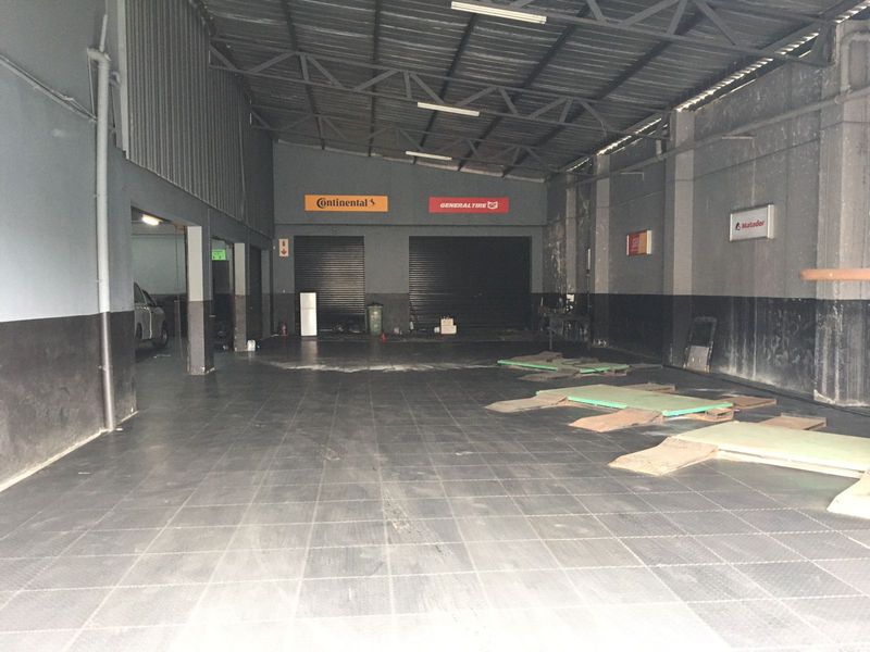 Spacious commercial garage or workshop area featuring high ceilings with exposed steel trusses, roller shutter doors, and durable tiled flooring.