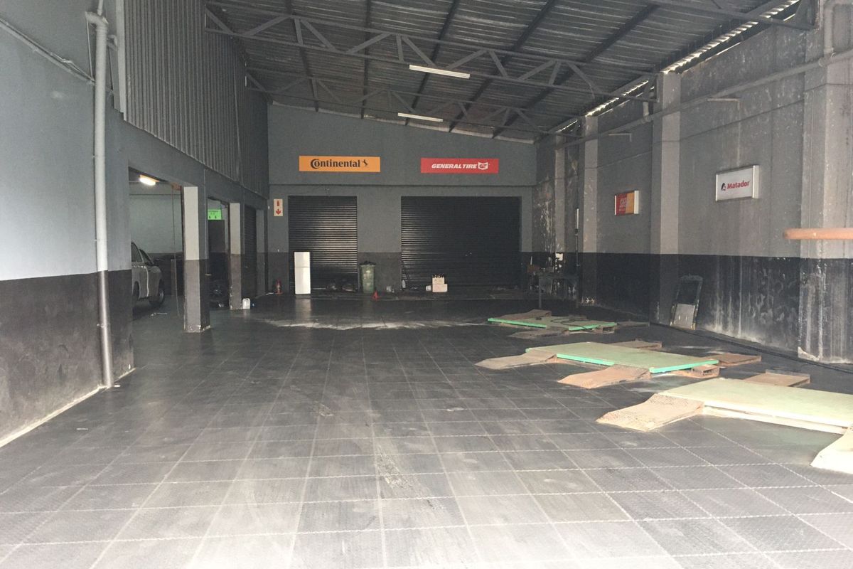 Spacious commercial garage or workshop area featuring high ceilings with exposed steel trusses, roller shutter doors, and durable tiled flooring.