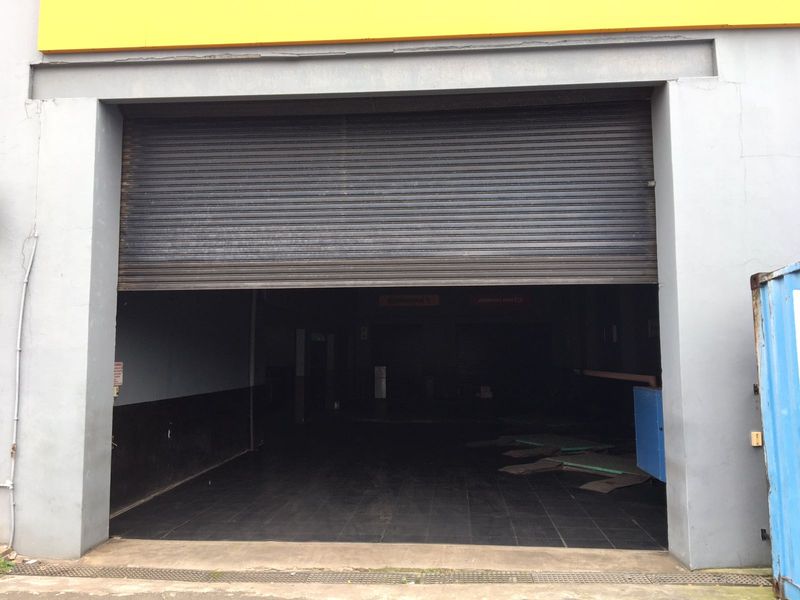 Commercial garage space featuring a large roller shutter door and tiled flooring, suitable for workshop or storage use.