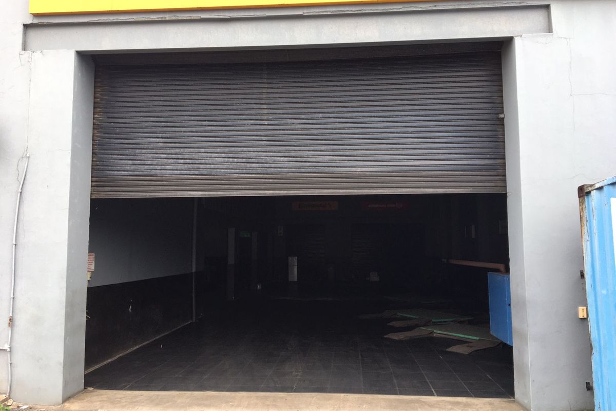 Commercial garage space featuring a large roller shutter door and tiled flooring, suitable for workshop or storage use.