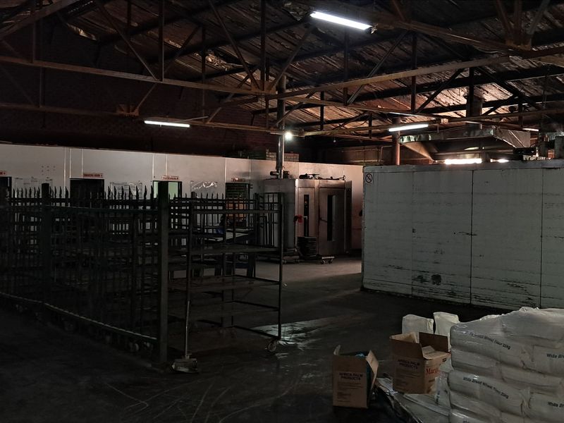 Industrial utility space featuring exposed steel roof trusses, concrete flooring, and integrated walk-in cold storage units suitable for manufacturing or food processing operations.