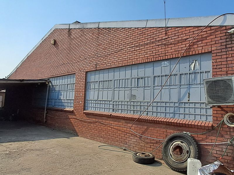 Rear exterior view of an industrial brick building featuring a covered parking area, security-barred windows, and an external air conditioning unit.