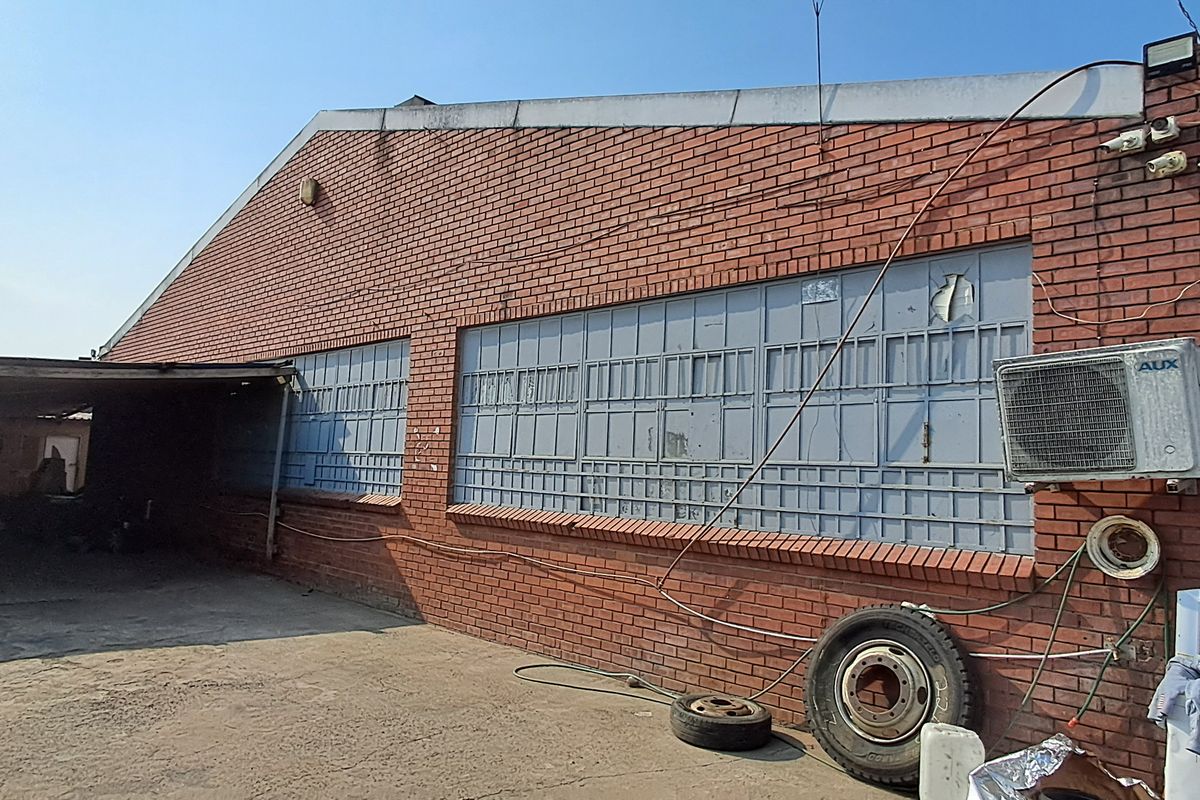 Rear exterior view of an industrial brick building featuring a covered parking area, security-barred windows, and an external air conditioning unit.