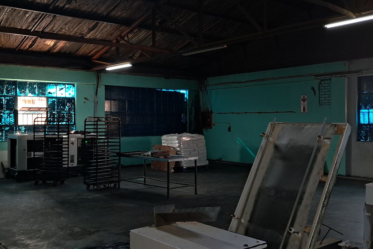 Spacious industrial utility area featuring exposed timber roof trusses, concrete flooring, and large steel-framed windows, suitable for manufacturing or storage operations.