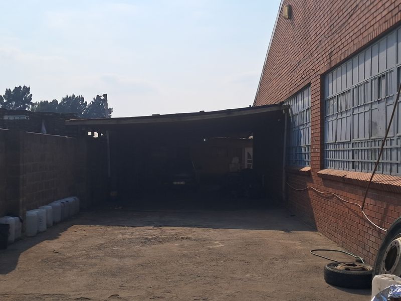 Rear industrial yard featuring a covered loading area, brick boundary wall, and external air conditioning unit mounted on the brick facade.