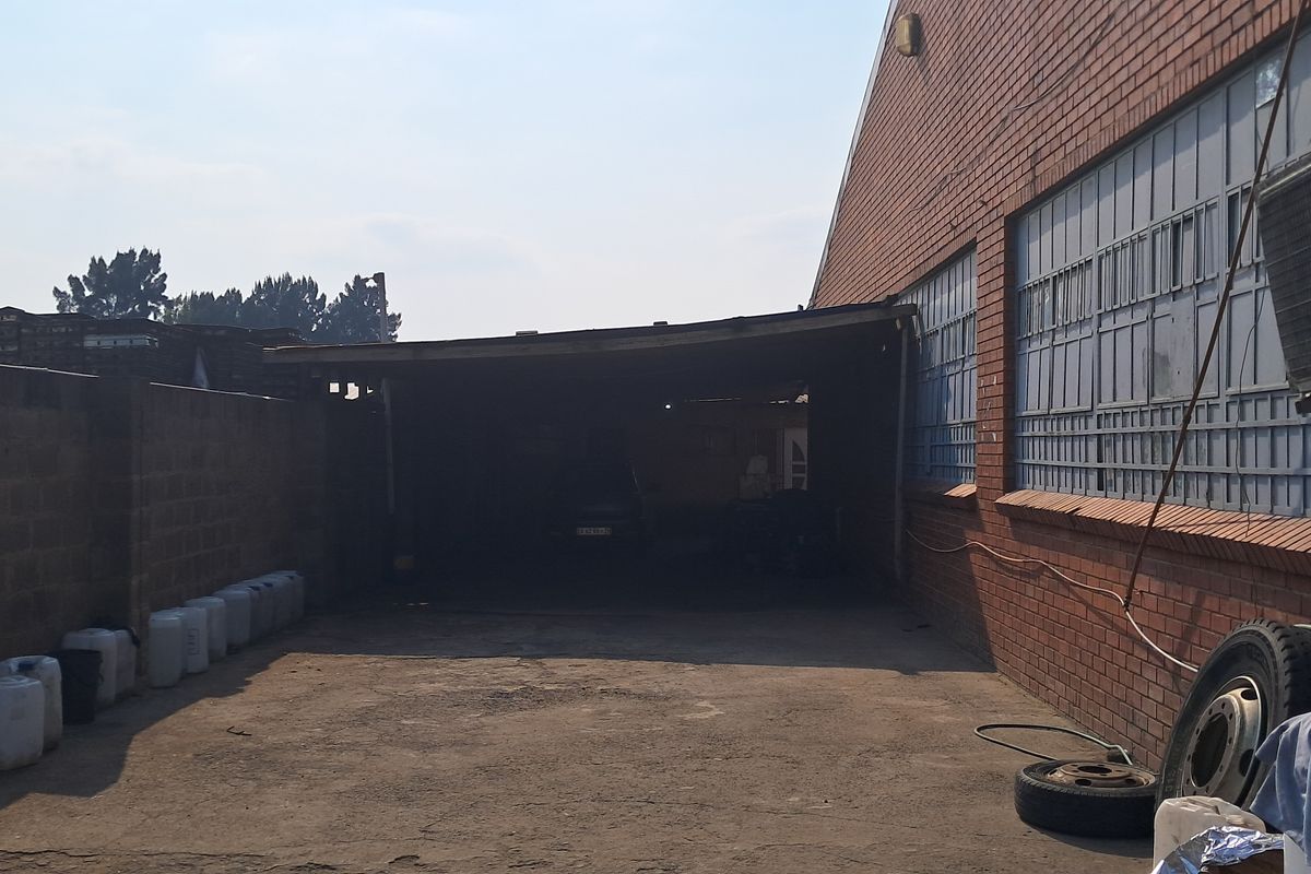 Rear industrial yard featuring a covered loading area, brick boundary wall, and external air conditioning unit mounted on the brick facade.