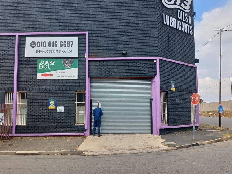 Front elevation of an industrial property featuring a roller shutter door, security bars, and prominent commercial signage.