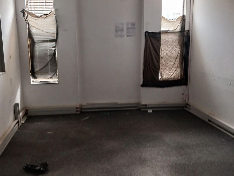 An empty office space featuring worn carpeting, scuffed walls, and damaged window blinds, requiring refurbishment to restore its professional utility.