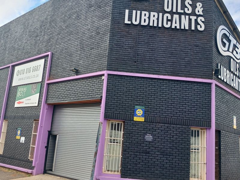 Industrial property facade featuring a roller shutter door, security bars, and prominent branding signage on a dark brick exterior.