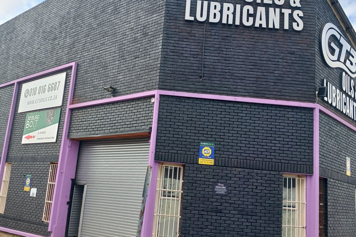 Industrial property facade featuring a roller shutter door, security bars, and prominent branding signage on a dark brick exterior.