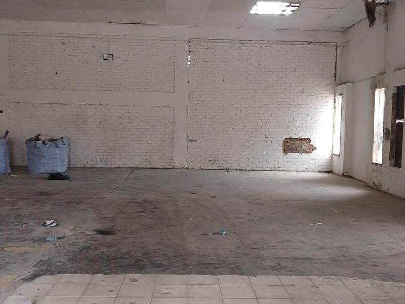 An empty industrial utility space featuring exposed brick walls, a mix of concrete and tiled flooring, and damaged ceiling infrastructure.