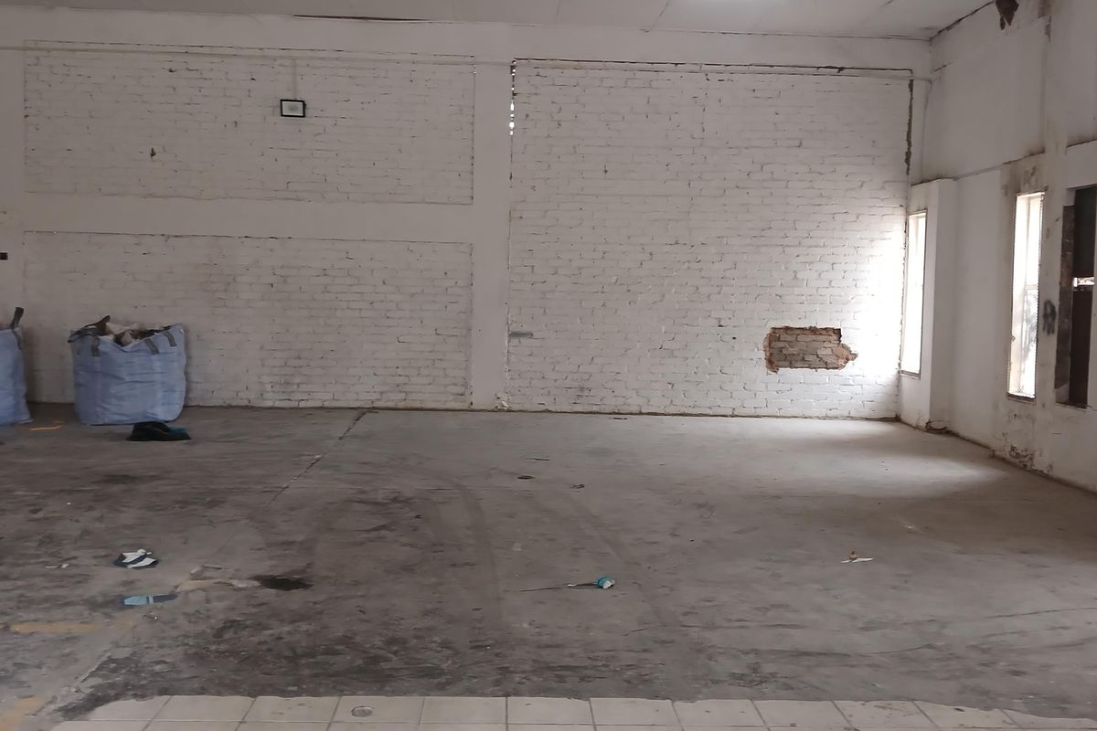 An empty industrial utility space featuring exposed brick walls, a mix of concrete and tiled flooring, and damaged ceiling infrastructure.