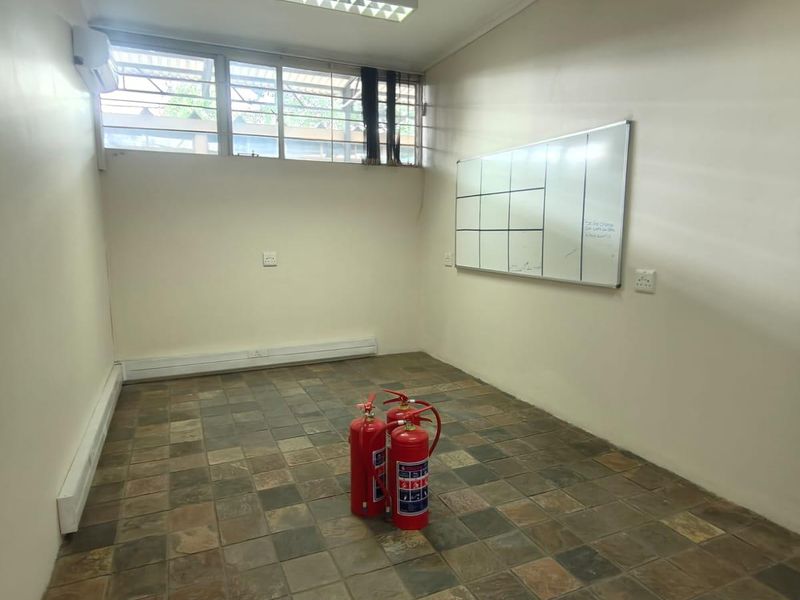A functional office space featuring slate tile flooring, a wall-mounted whiteboard, air conditioning, and an exposed timber beam detail.