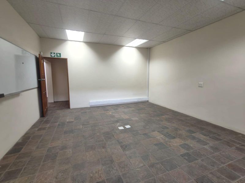 A vacant office space featuring tiled flooring, a suspended ceiling with recessed lighting, and a wall-mounted whiteboard.