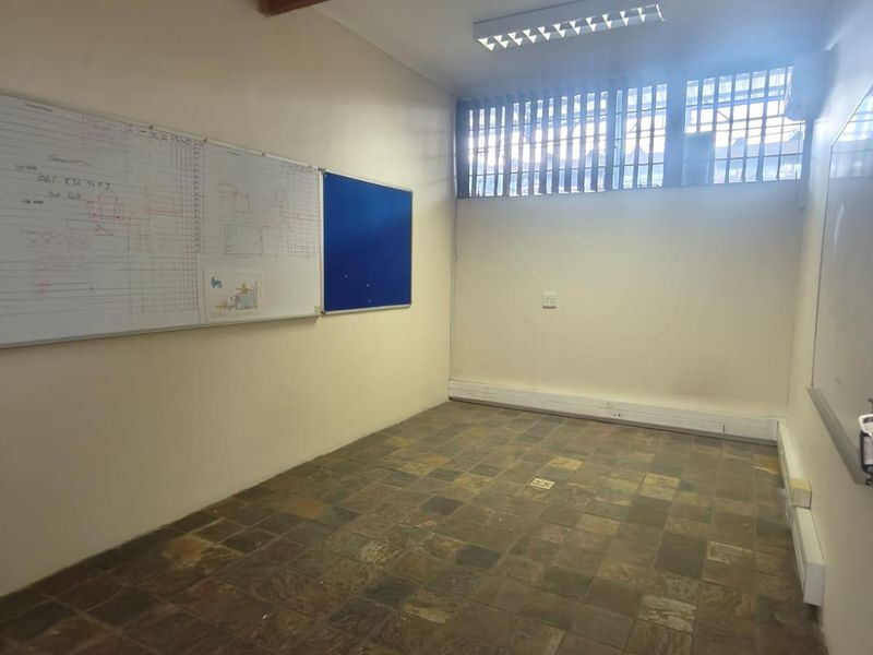 A functional office space featuring slate tile flooring, fluorescent lighting, and wall-mounted boards, offering a practical layout for a professional work environment.