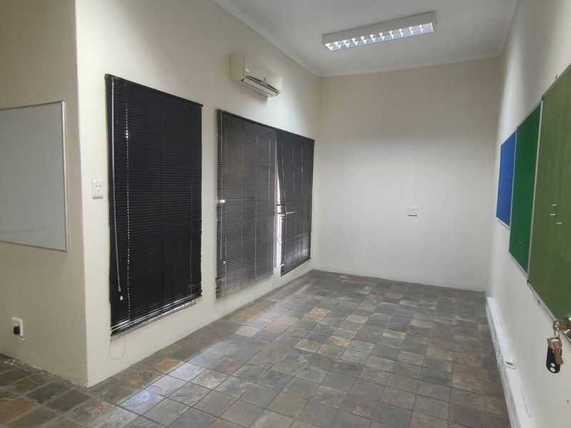 A functional office space featuring slate tile flooring, split-system air conditioning, venetian blinds, and wall-mounted notice boards, suitable for a professional work environment.