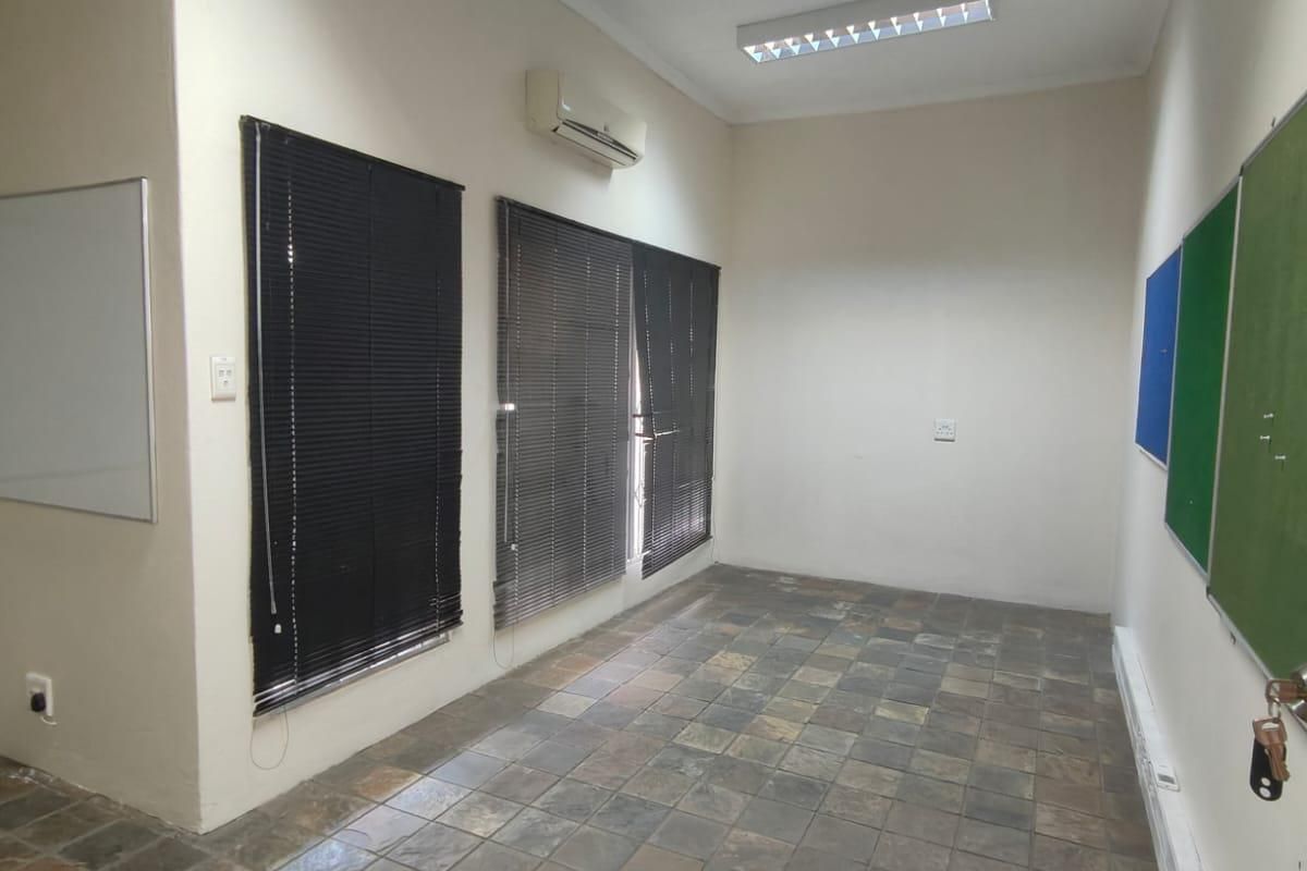 A functional office space featuring slate tile flooring, split-system air conditioning, venetian blinds, and wall-mounted notice boards, suitable for a professional work environment.