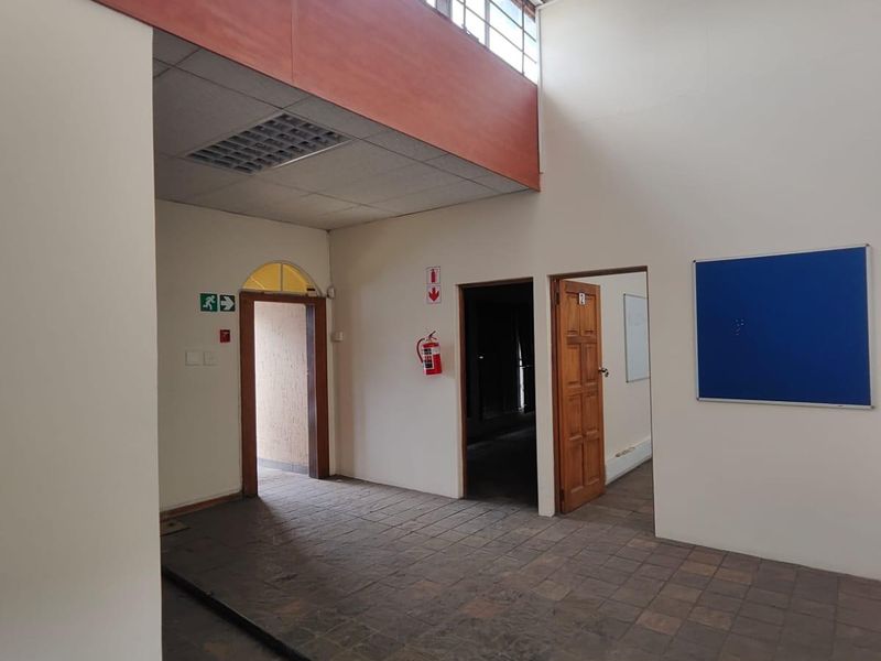 Spacious office interior featuring high-level clerestory windows, tiled flooring, and multiple access points, providing a functional and well-lit workspace environment.