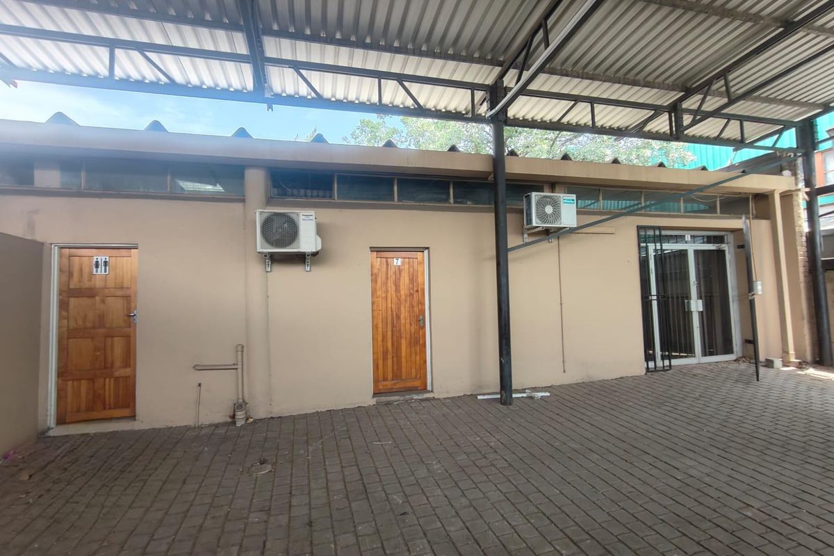 Exterior view of an office building rear area featuring a covered paved courtyard, multiple access doors, and wall-mounted air conditioning units.